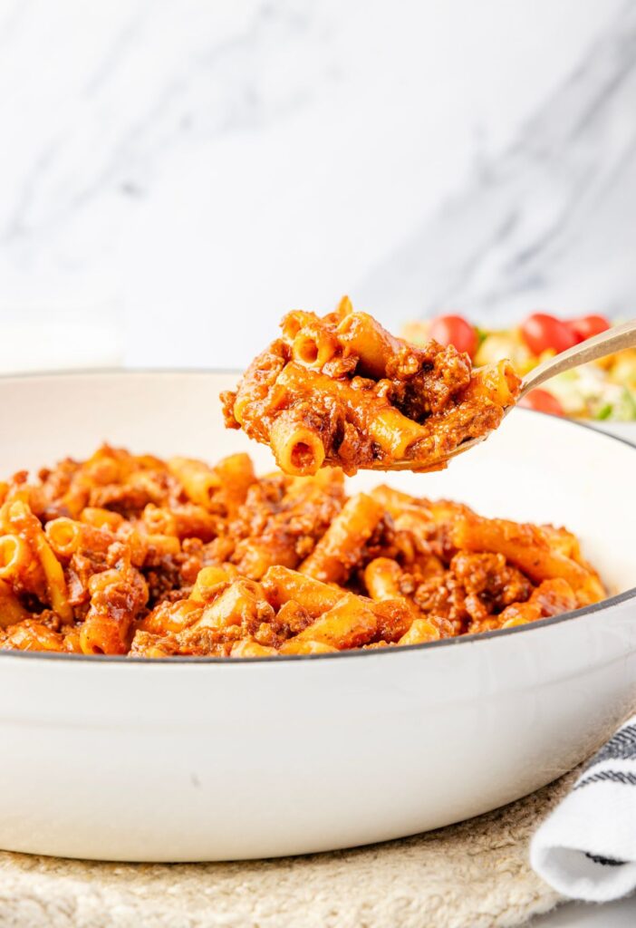 Scoop of the beefaroni above the skillet pan
