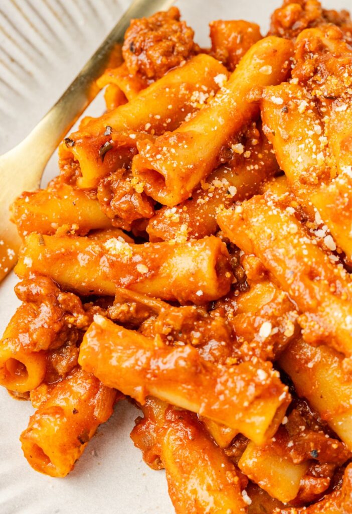 A serving of beefaroni on a white plate and fork in it.