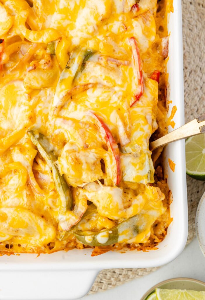Cheesy fajita chicken casserole with rice and a serving spoon inside of it.
