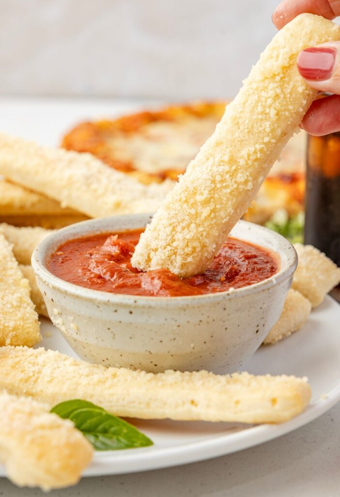 A breadstick being dipped into a bowl of red marinara sauce