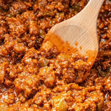 A crockpot with a wooden spoon and the sloppy Joe meat mixture.