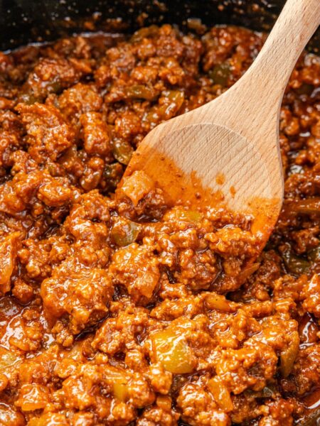 A crockpot with a wooden spoon and the sloppy Joe meat mixture.