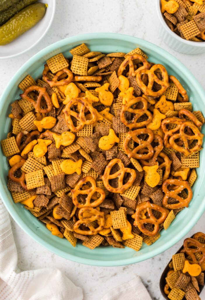 Bowl of savory chex mix with a dill pickle next to it.