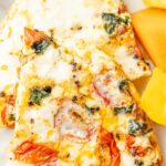 Egg white frittata on a white plate with fresh fruit to the side.