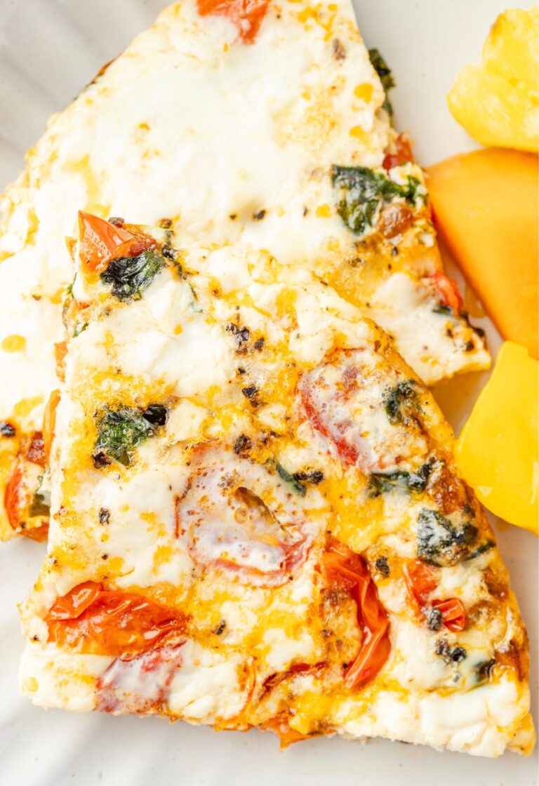 Egg white frittata on a white plate with fresh fruit to the side.