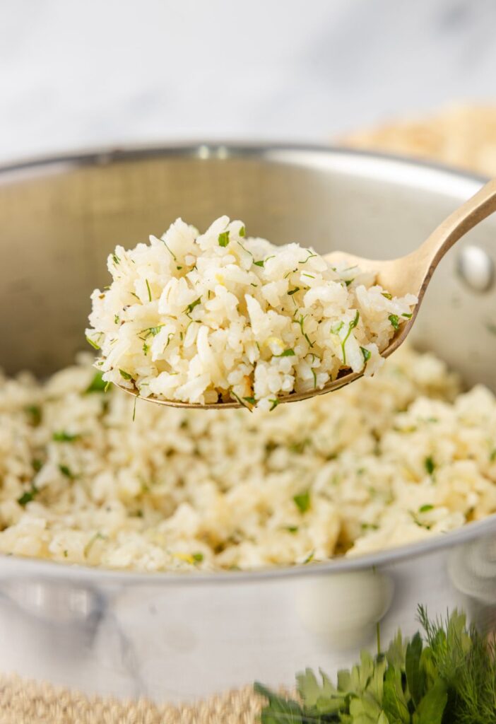 A pan of greek rice with a side view of a spoon serving some.