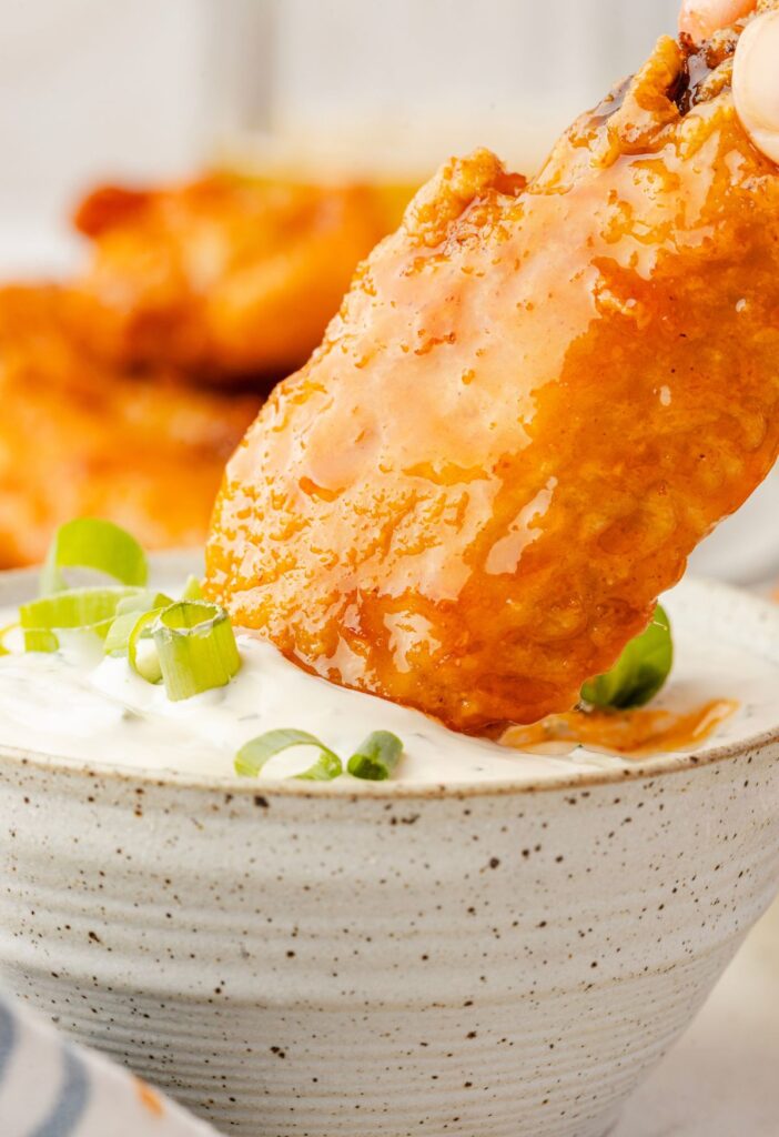 A buffalo hot honey wing being dipped into blue cheese dip