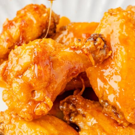 Honey being drizzled over top the chicken wings