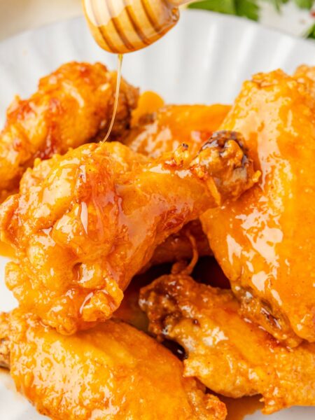 Honey being drizzled over top the chicken wings