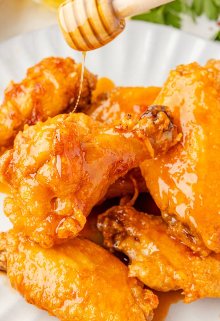 Honey being drizzled over top the chicken wings