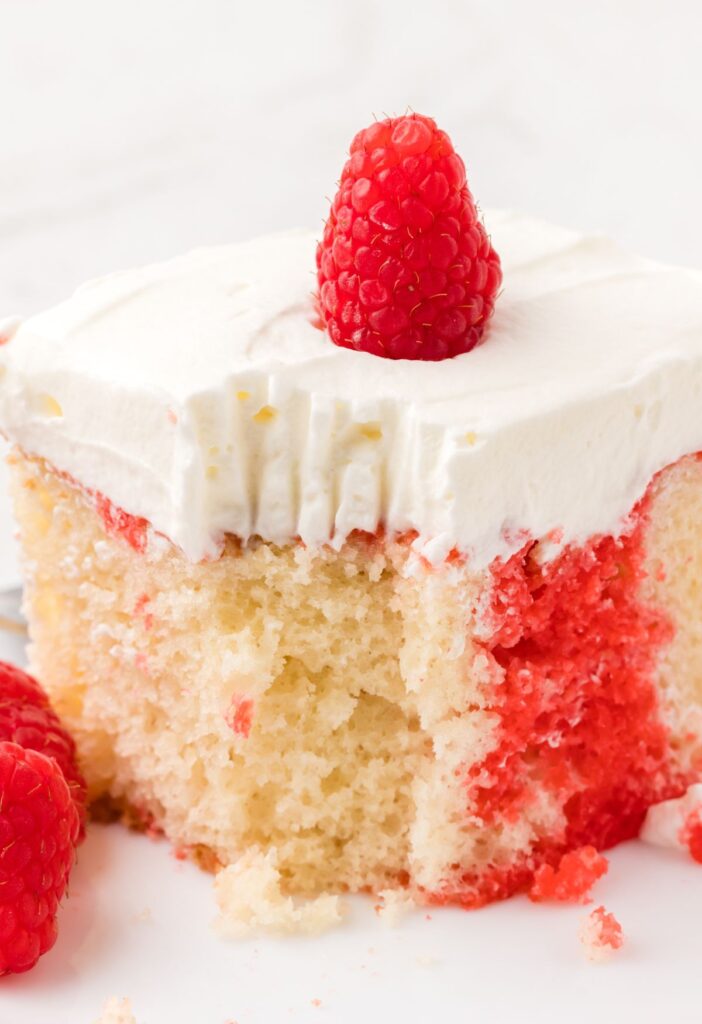 A slice of raspberry poke cake with a fork bite taken out of the front.