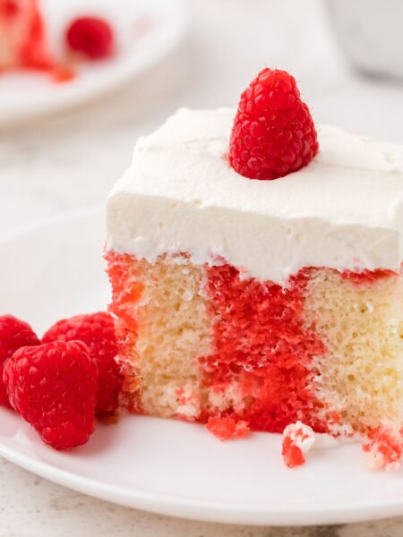 A slice of poke cake with a raspberry on top of whipped cream frosting.