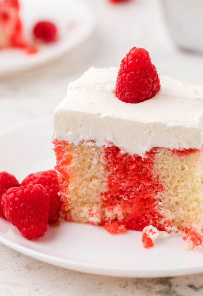 A slice of poke cake with a raspberry on top of whipped cream frosting.