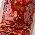 Loaf of baked meatloaf with a glaze and parsley sprinkle on top.