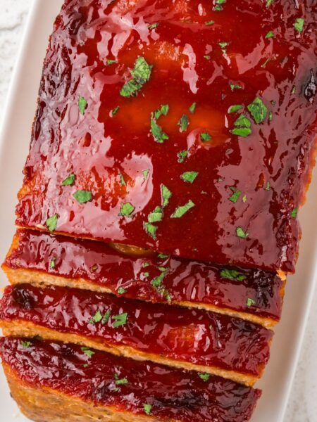 Loaf of baked meatloaf with a glaze and parsley sprinkle on top.