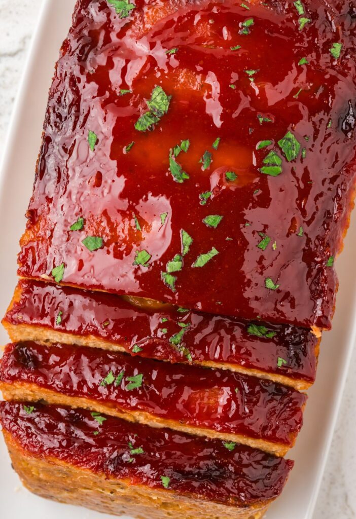 Loaf of baked meatloaf with a glaze and parsley sprinkle on top.
