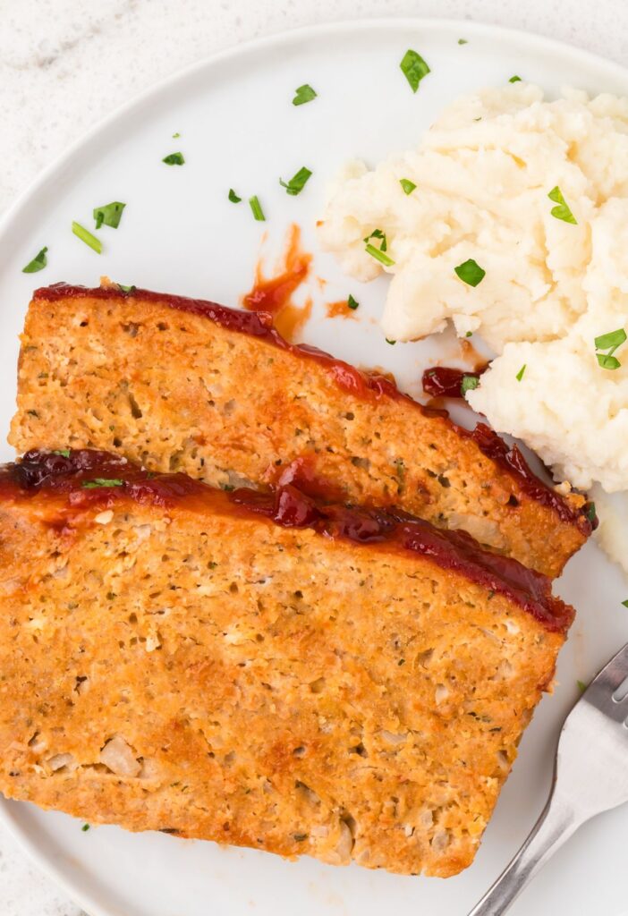 A serving of two slices of meatloaf on a plate with mashed potatoes.