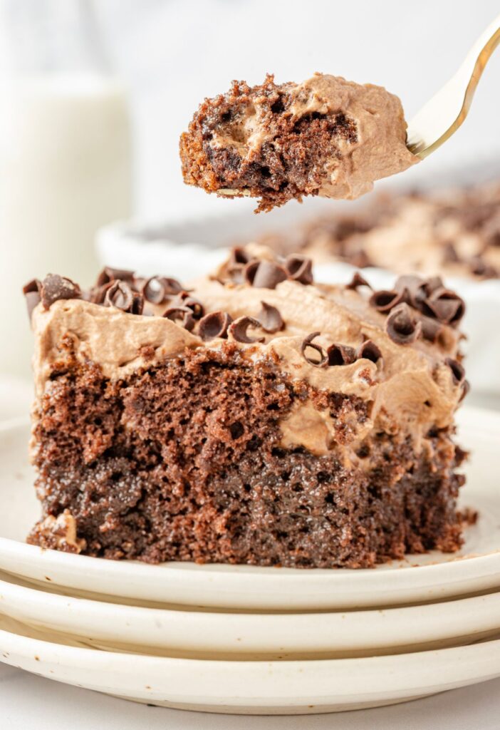 A slice of chocolate poke cake sitting on a stack of plate with a fork.