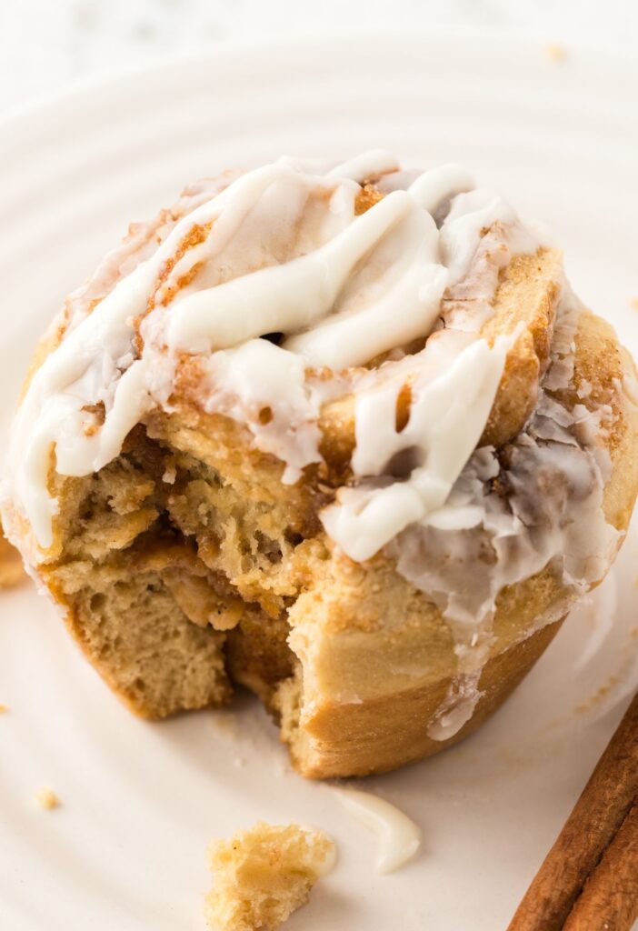 One cinnamon roll muffin on a white plate with a bite taken out of it.