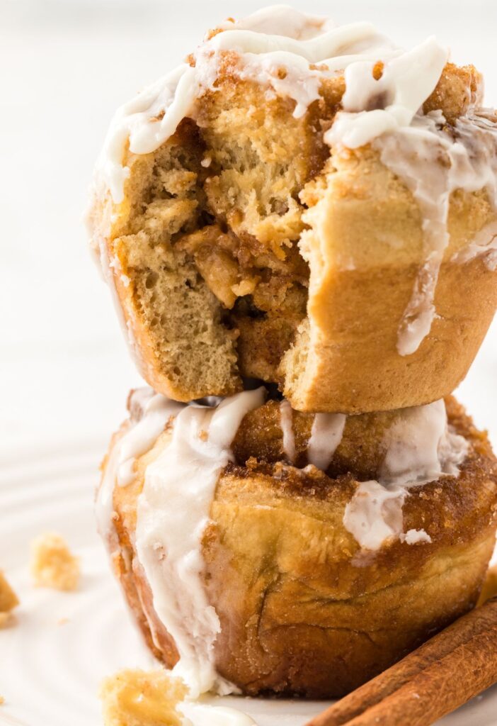 A stack of two cinnamon roll muffins with glaze, the top muffin has a bite taken out of it.