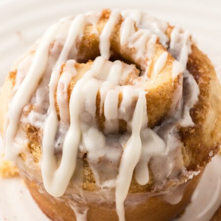 One cinnamon roll muffin that has been glazed sitting on a white plate.