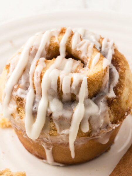 One cinnamon roll muffin that has been glazed sitting on a white plate.