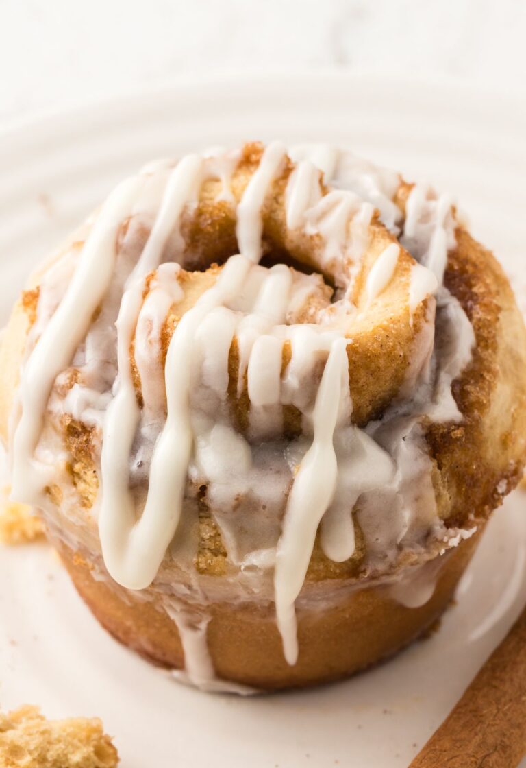 One cinnamon roll muffin that has been glazed sitting on a white plate.