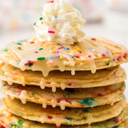 Stack of funfetti pancakes with whipped cream drizzled over and glaze.