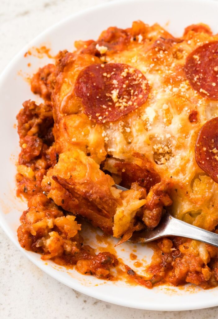 A serving of the pizza tater tot casserole on a white plate with a fork next to it.