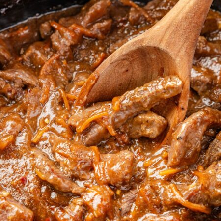 Inside of the slow cooker with the cooked beef in a wooden serving spoon.