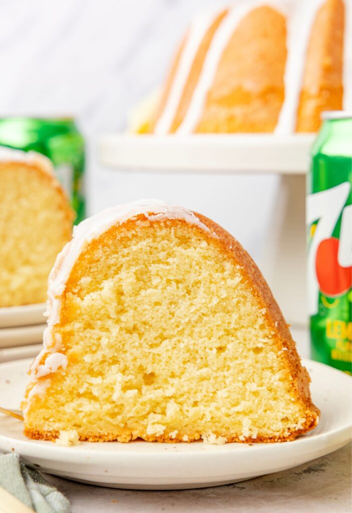A slice of the 7up cake on a white plate with a can of lemon lime 7 up soda in the background.