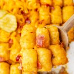 A casserole pan of the tater tot casserole with a wooden serving spoon with a scoop on it.