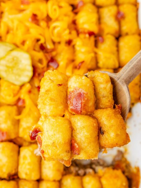 A casserole pan of the tater tot casserole with a wooden serving spoon with a scoop on it.