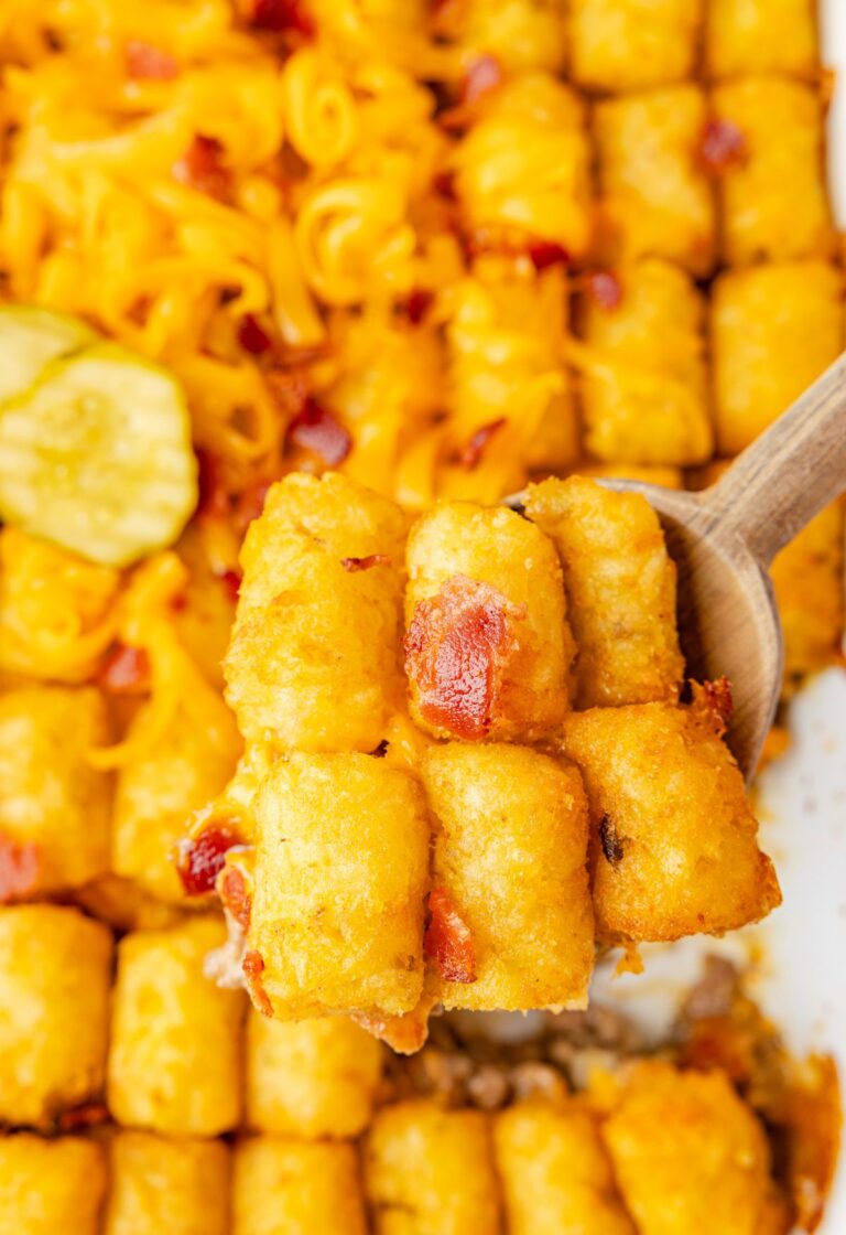 A casserole pan of the tater tot casserole with a wooden serving spoon with a scoop on it.