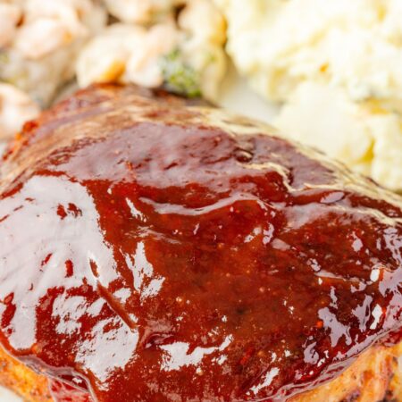 A barbecue chicken thigh with extra bbq sauce on it on a plate with some macaroni salad.