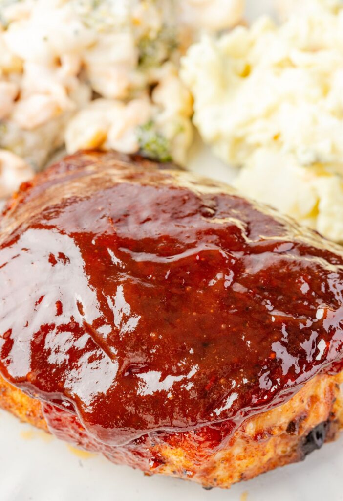 A barbecue chicken thigh with extra bbq sauce on it on a plate with some macaroni salad.