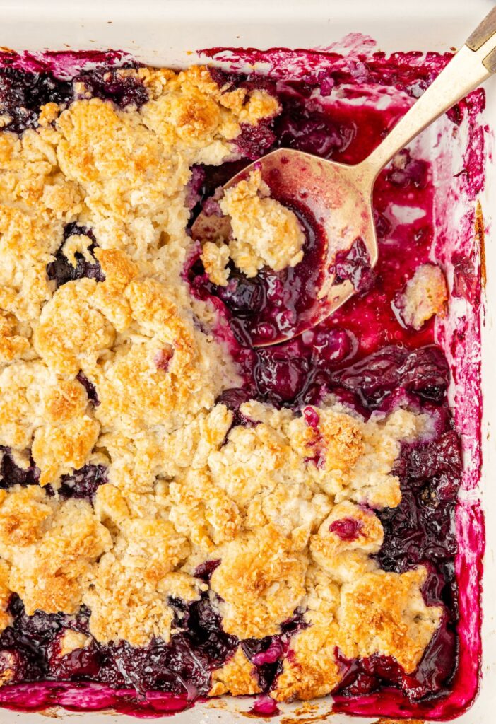 A top view of the blueberry crumble inside the baking pan with a serving spoon.