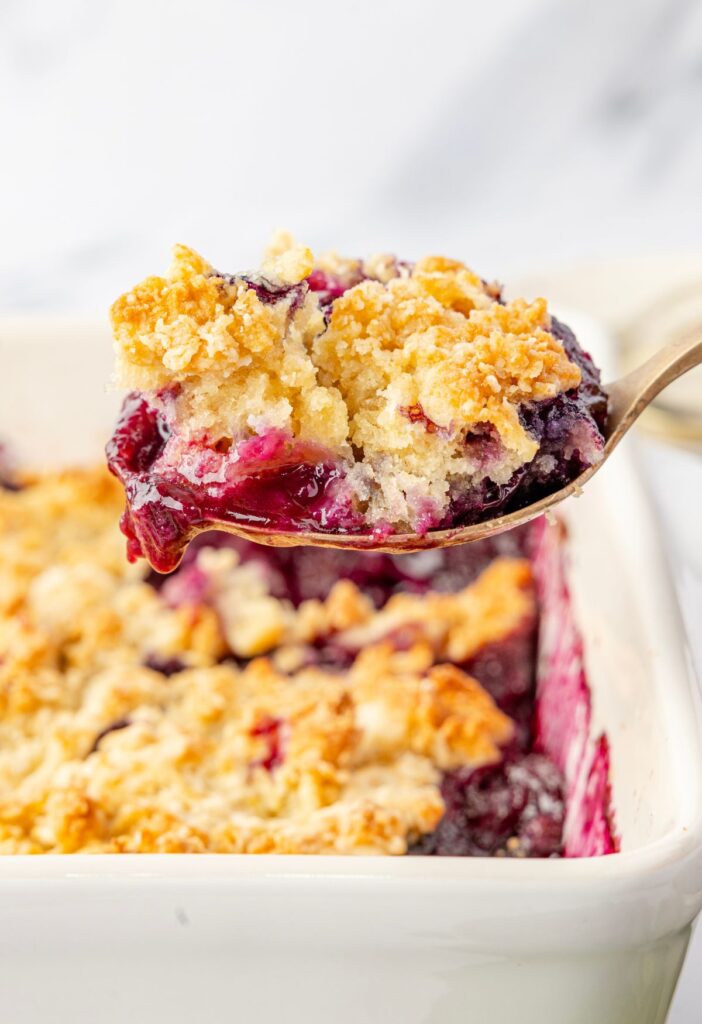 A scoop of the blueberry crumble above the pan of the dessert.