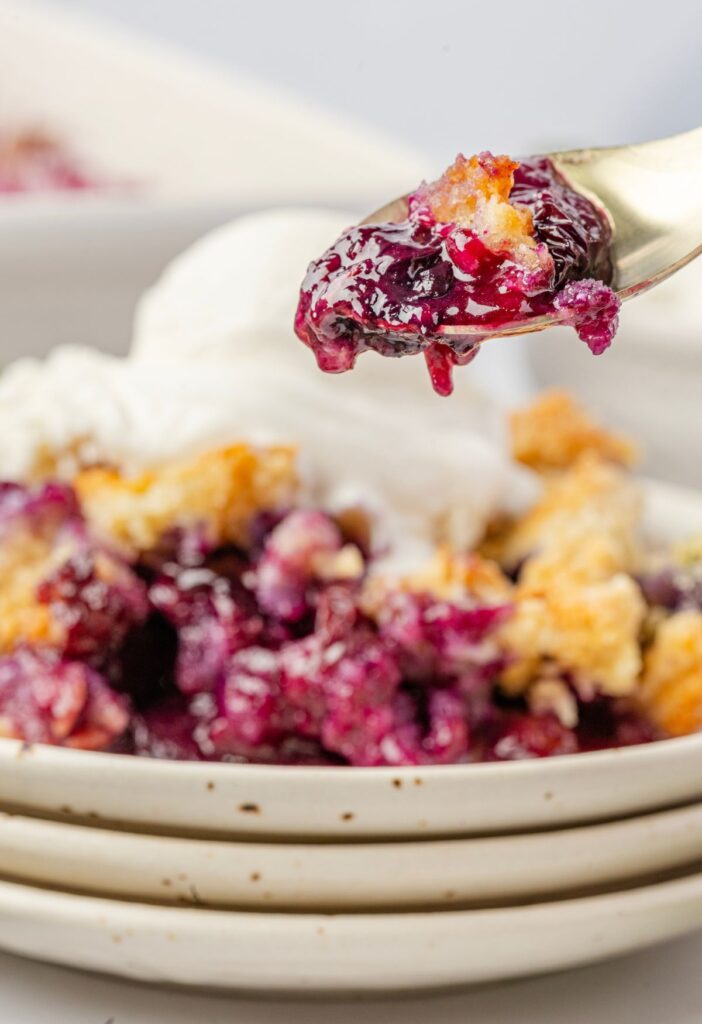 A serving of blueberry crumble on a stack of plates with a spoon with some on it.