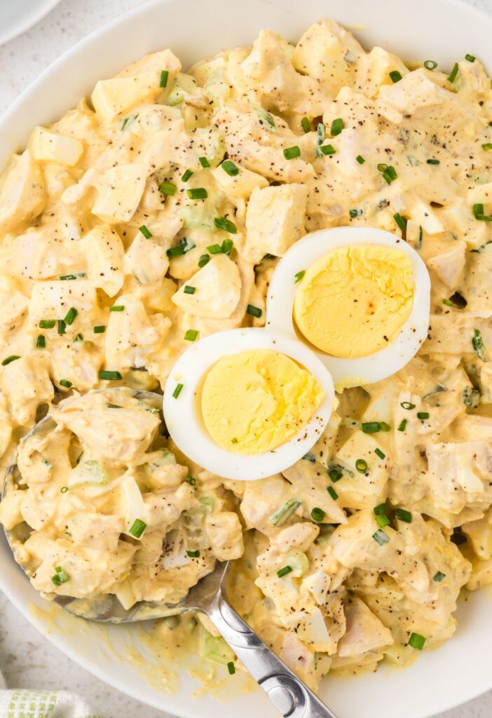 Chicken salad with deviled eggs inside a bowl with a serving spoon.