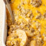 A casserole pan with the potato and beef casserole inside of it with a serving spoon.