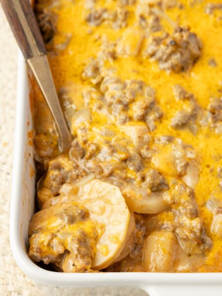 A casserole pan with the potato and beef casserole inside of it with a serving spoon.