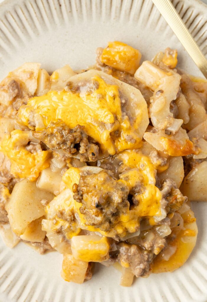 A serving of potato casserole with cheese on a white plate.