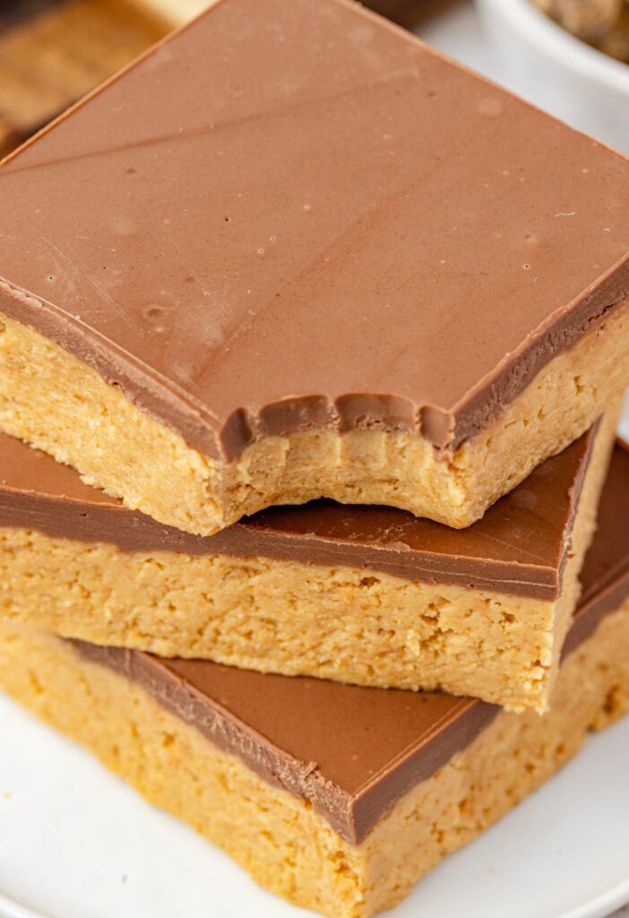 A stack of chocolate peanut butter bars with the top one with a bite taken out of it