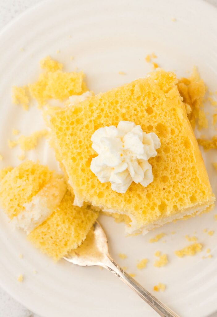 A top view of the slice of yellow sponge cake for the Twinkie Cake on a white plate with a fork.