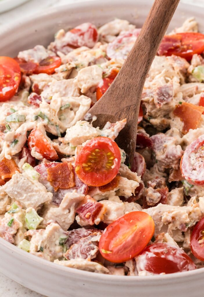 A bowl of blt chicken salad with a wooden serving spoon