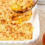 Side view of a scoop of cobbler above the pan of peach cobbler