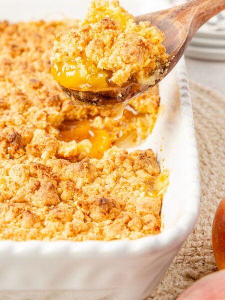 Side view of a scoop of cobbler above the pan of peach cobbler
