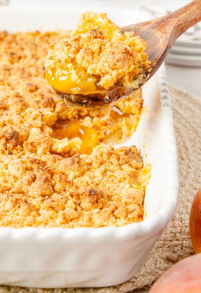 Side view of a scoop of cobbler above the pan of peach cobbler