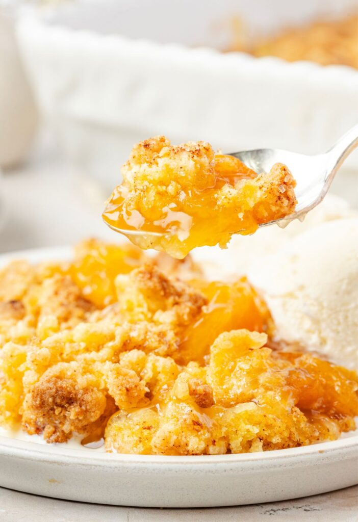 A serving of the peach cobbler with ice cream and a spoon with some cobbler on it.